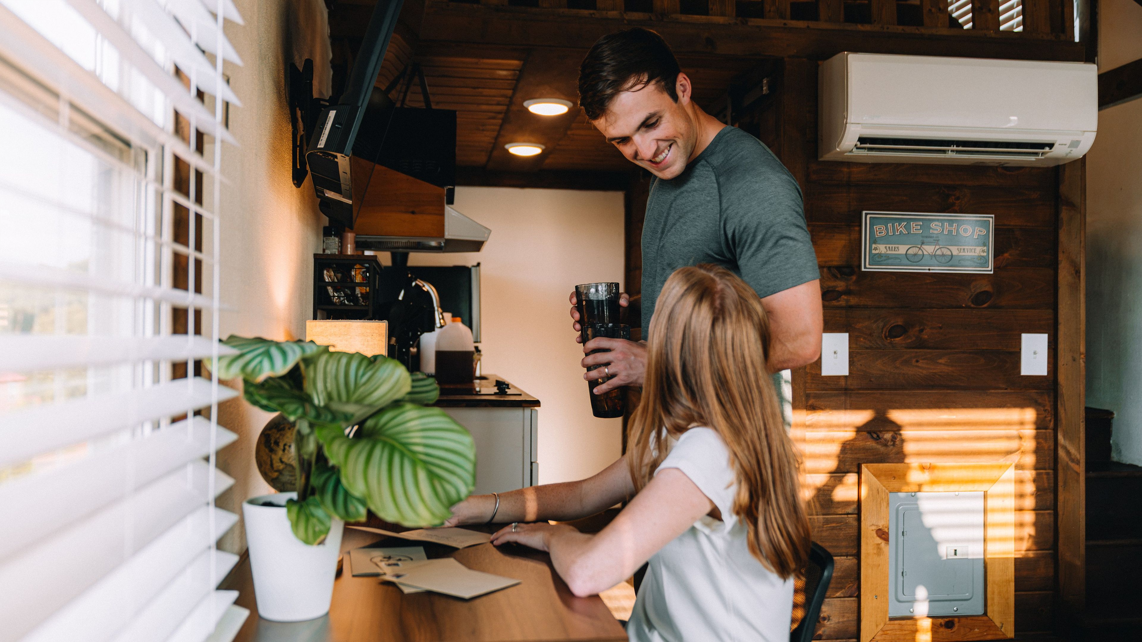 A person handing over a document to another person in a room with wooden walls, a sign indicating a bike shop, and a potted plant.
