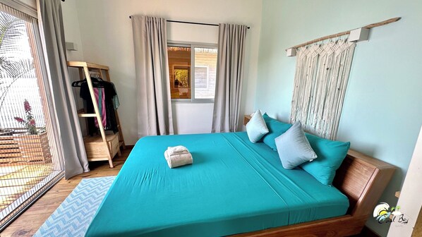 Un dormitorio con cama, un armario de madera, un colgador de macramé y vistas al exterior.