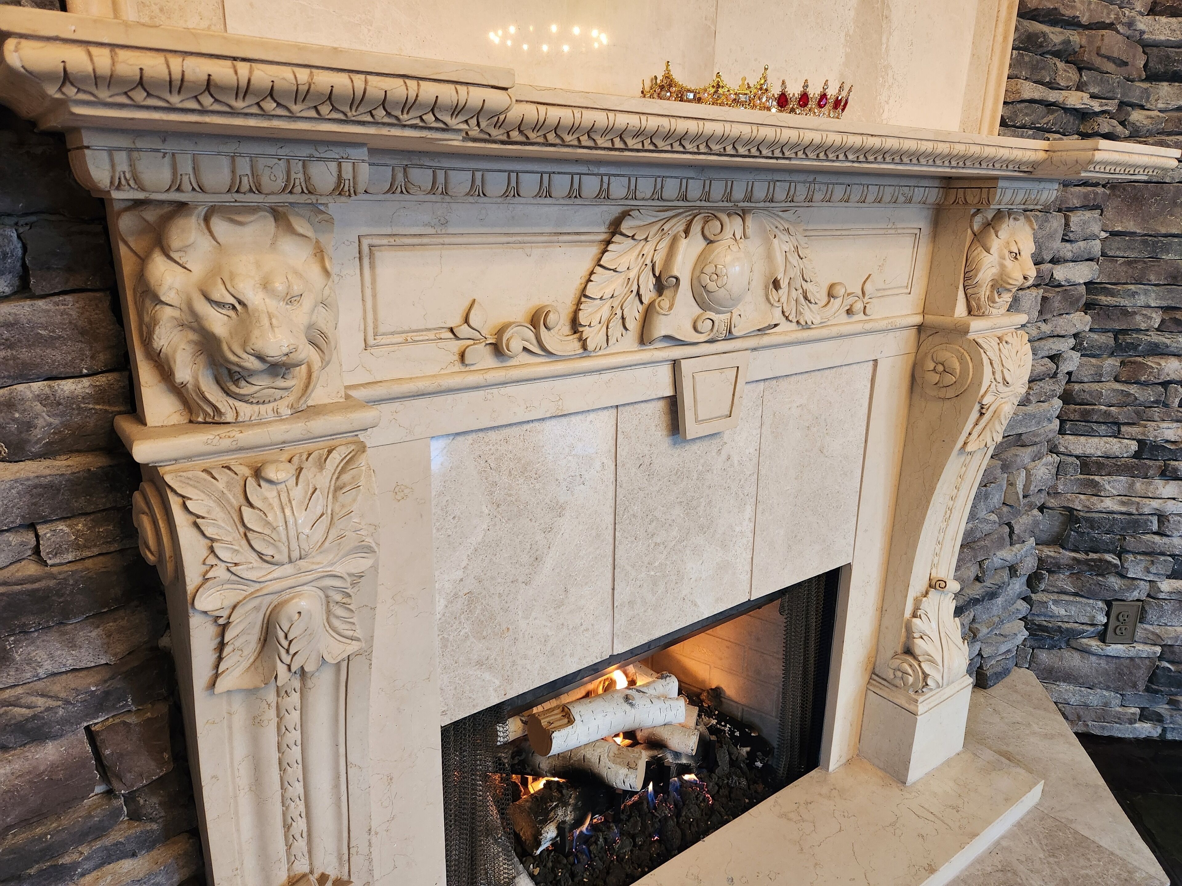 A fireplace with intricate carvings, a stone wall, and a crown above it.