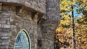 Un bâtiment en pierre doté d’une tourelle et d’une fenêtre en arc de cercle, entouré d’arbres aux feuilles d’automne.