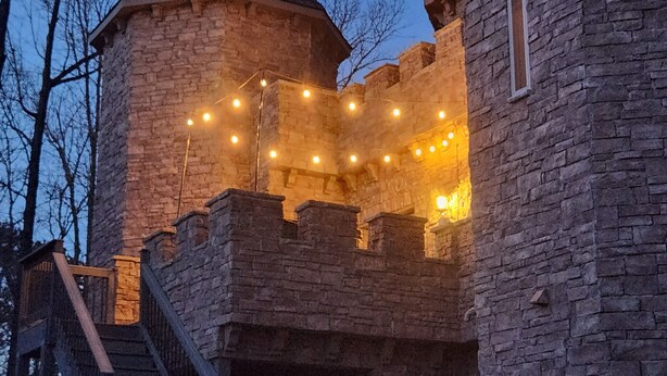 Un château en pierre doté d’une tourelle et d’un escalier menant à un balcon.