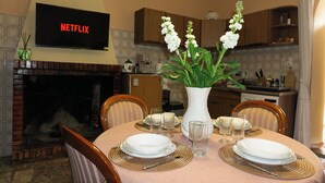 A dining room with a fireplace, a TV mounted above it displaying "NETFLIX", and a table set with plates, glasses, and a vase with flowers. - La Casa Borgo Ischia di Castro (Ischia di Castro)