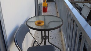 A small balcony with a round table and two chairs, a red bucket, and a yellow object on the table. - Patisia Metro Station 2 bdrm apartment by MPS (Athina)
