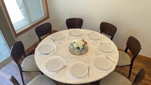 A round dining table with white plates, silverware, and glasses, surrounded by dark wooden chairs with grey cushions. - Charming 3-bedroom Sunriver house with WiFi, AC hot tub, bikes, kayak, grill (Sunriver)