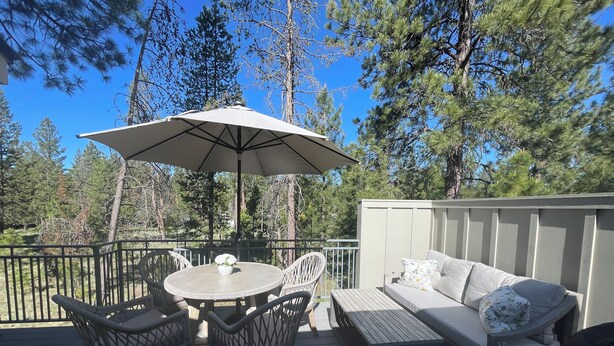A deck with a table and chairs, a sofa, and an umbrella. - Charming 3-bedroom Sunriver house with WiFi, AC hot tub, bikes, kayak, grill (Sunriver)