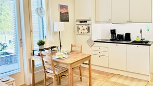 A modern kitchen with white cabinets, a wooden dining table, and a small island with a lamp. - Brand-new studio surrounded by forest, All New Cozy Home in Turku (Turku)