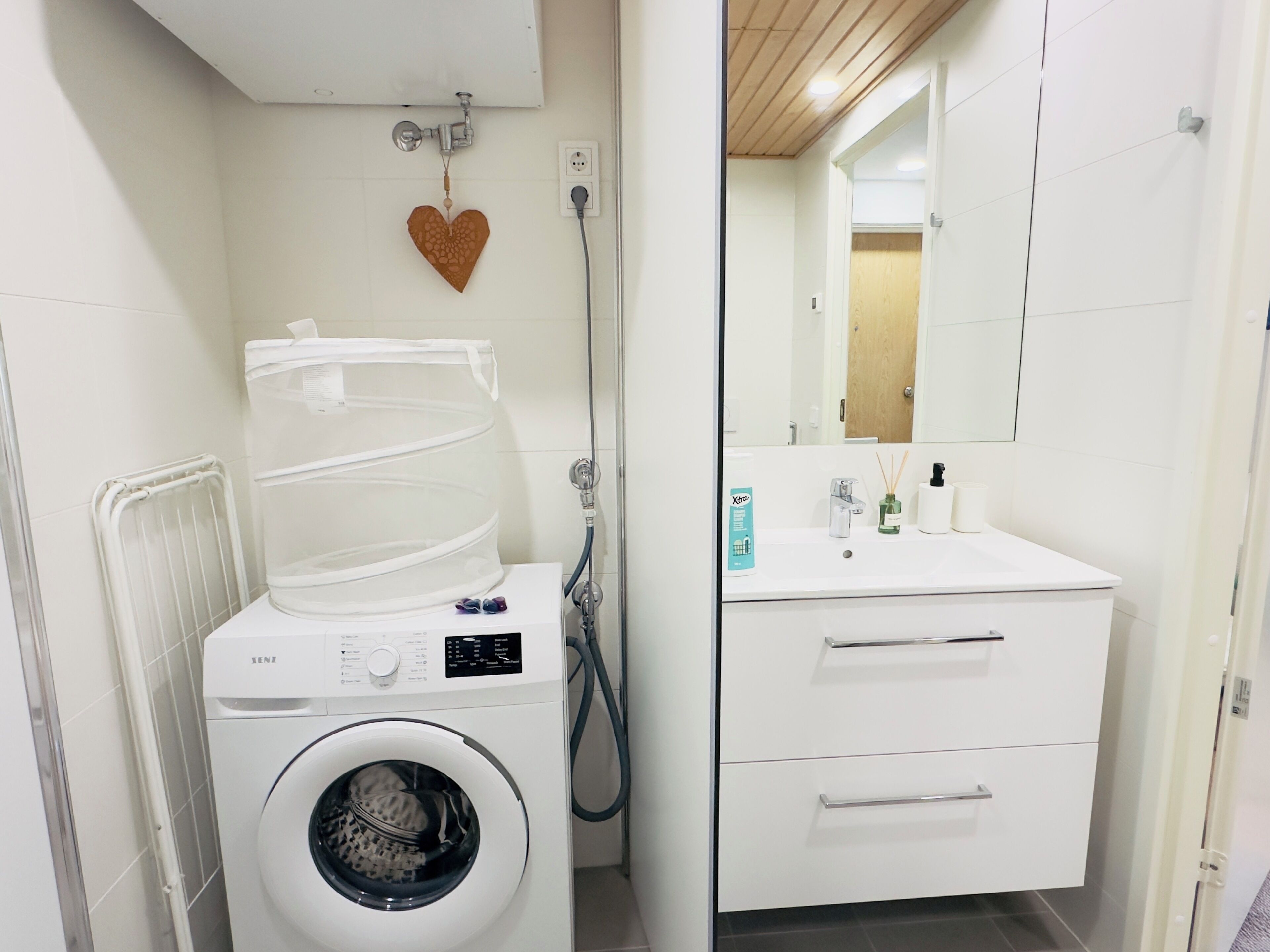 Un espace buanderie compact comprenant un lave-linge, un étendoir et un évier avec des produits de toilette.