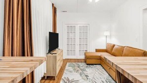 A modern living room with a wooden dining table, a leather sofa, and a flat-screen TV. - Historic Uptown w/2x Parking & Patio pet-friendly (St. Petersburg)