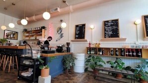 A cafe interior with a bar area, seating, and a counter where a person is preparing a drink. - Historic Uptown w/2x Parking & Patio pet-friendly (St. Petersburg)