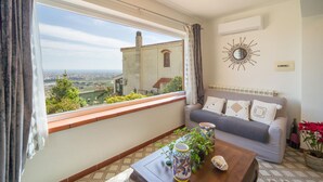 Un accogliente soggiorno con divano, un tavolino da caffè con oggetti decorativi, vista sulla città attraverso una finestra e uno specchio decorativo appeso al muro.