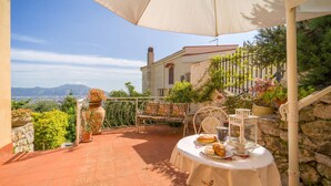 Una terrazza con un tavolo apparecchiato per un pasto, una sedia e una pianta in vaso.