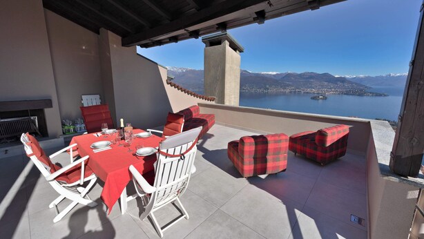 An outdoor patio with a table set for dining, red and white chairs, and a view of a lake and mountains. - Eco-friendly design, modern comforts and a prime scenic location (Someraro)