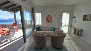 A modern living room with a beige sofa, two armchairs, and a coffee table. There is a large window with a view of the sea and mountains. - Eco-friendly design, modern comforts and a prime scenic location (Someraro)