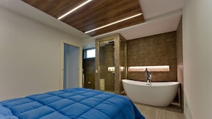 A modern bedroom with a large bed, a freestanding bathtub, and a walk-in shower. - Eco-friendly design, modern comforts and a prime scenic location (Someraro)