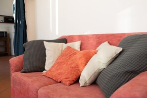 A red sofa with multiple cushions in various textures and colors.