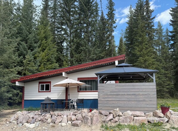 A cabin with a covered patio, outdoor seating, and a stone wall.