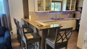 Una cocina compacta con una isla central, armarios de madera y una zona de comedor con sillas.