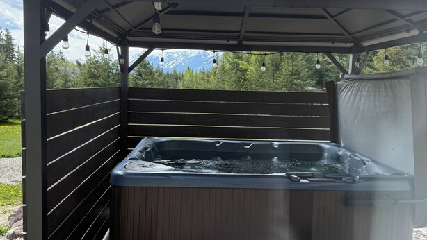 Un jacuzzi bajo una pérgola de madera con vistas a las montañas.