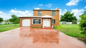 A two-story house with a red driveway, a garage, and a front porch. - Spacious & Expansive Miami Home With Free Parking (Homestead)