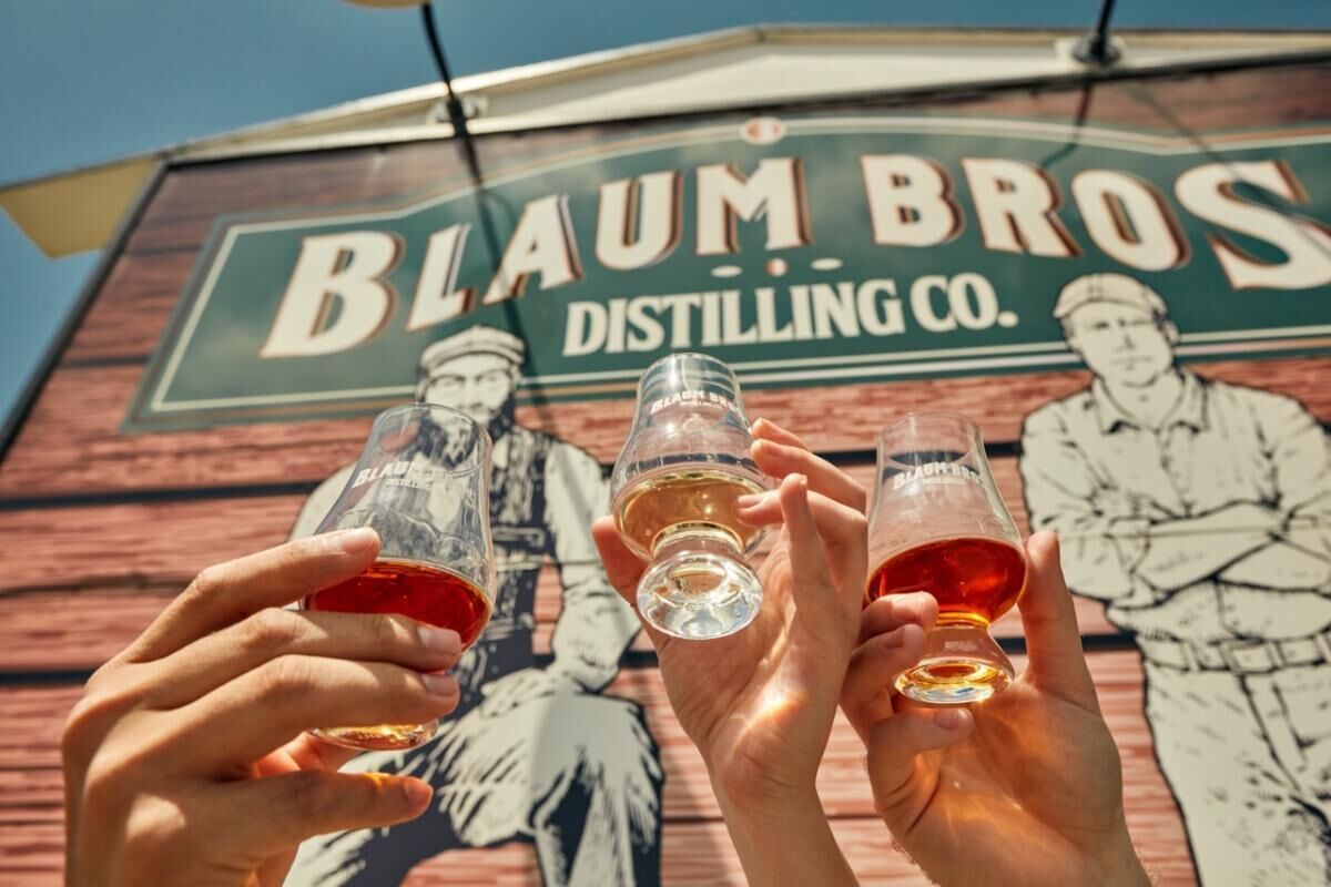 A sign for Blaum Bros Distilling Co. with three people toasting.