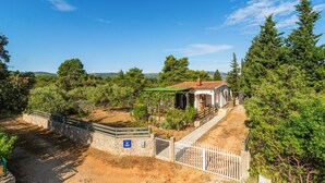 A rustic house with a tiled roof, surrounded by dense greenery and a stone wall.
