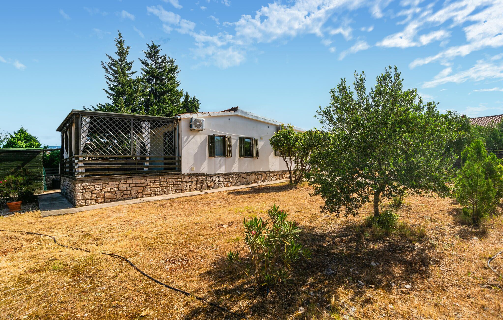 Uma casa branca com base de pedra, área externa cercada e um campo de grama seca.