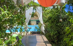 Un sentier mène à une piscine bordée d’une végétation luxuriante et agrémentée de tentures blanches.