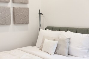Un lit avec une literie blanche, une tête de lit grise et une lampe fixée au mur.