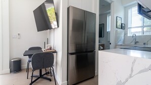 A modern kitchen with a large stainless steel refrigerator, a dining area with a table and chairs, and a view of the outdoors through a window.