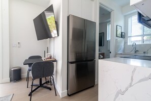 A modern kitchen with a large stainless steel refrigerator, a dining area with a table and chairs, and a view of the outdoors through a window.