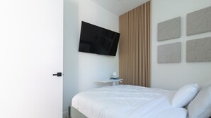 A modern bedroom with a bed, a TV mounted on the wall, and a small bedside table.