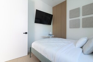 A modern bedroom with a bed, a TV mounted on the wall, and a small bedside table.
