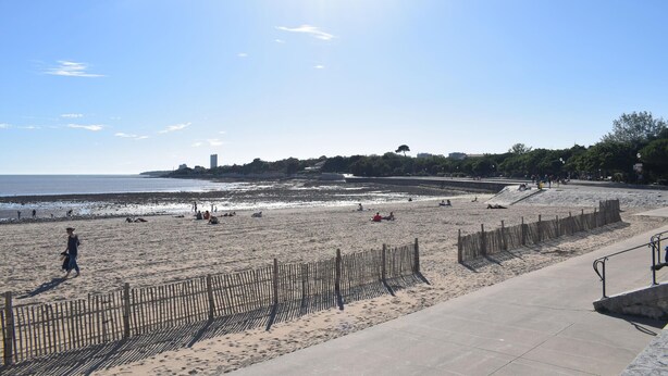 A beach with a wooden fence, a concrete walkway, and a distant view of buildings and trees. - Magnifique app à la Rochelle (La Rochelle)