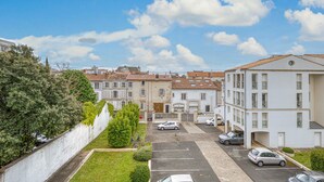 A residential street with parked cars, a white building with a balcony, and a tree-lined wall. - Magnifique app à la Rochelle (La Rochelle)