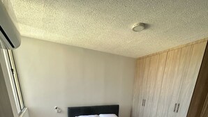 Quarto com cama, mesa de cabeceira, guarda-roupa e luz no teto.
