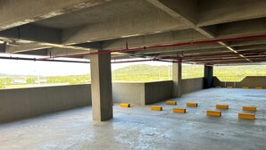 Garagem de estacionamento vazia, com pilares de concreto, defensas amarelas e canos visíveis.
