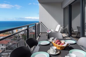 A balcony with a table set for breakfast, chairs, and a view of the ocean. - Flat in Funchal with Sea View - Amparo II (Funchal)