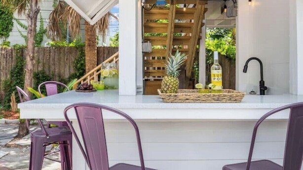 A kitchen with a white countertop, purple chairs, a wooden rack with bottles, and a pineapple. - Historic Uptown 2BD w/Shared Patio Pet-friendly (St. Petersburg)