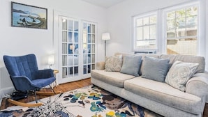 A living room with a sofa, a rocking chair, a patterned rug, and a painting on the wall. - Historic Uptown 2BD w/Shared Patio Pet-friendly (St. Petersburg)