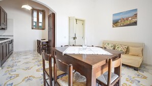 A dining area with a wooden table, chairs, and a vase. There is a kitchen area with cabinets and a stove. A door leads to another room.