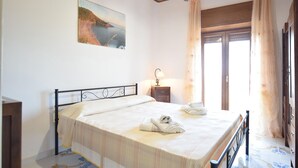A bedroom with a bed, a nightstand, a lamp, a painting, and a window with curtains.