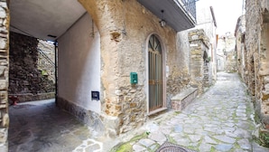 A narrow cobblestone street with stone buildings, a metal gate, and a manhole cover.