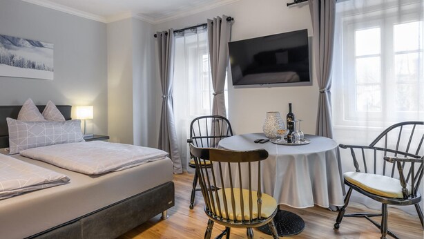 Een hotelkamer met een bed, twee stoelen, een tafel met een fles en glazen, en een televisie aan de muur.