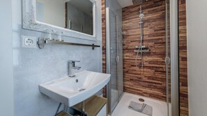 Een moderne badkamer met een witte wastafel, een grote spiegel en een douche met een houten wandpaneel.