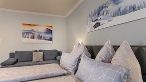 Een slaapkamer met een bed, een grijze bank en twee schilderijen aan de muur.