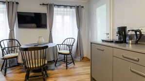 Een kleine, goed verlichte kamer met een ronde tafel, twee stoelen, een koffiezetapparaat en een televisie aan de muur.