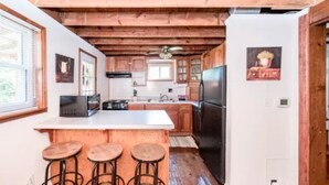A kitchen with wooden beams, a central island with stools, and a refrigerator.