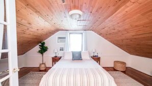A bedroom with a sloped ceiling, a large bed, two bedside tables, a window, and a potted plant.
