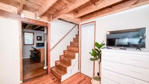 A wooden staircase leading to a dining area, a white dresser with a television, and a potted plant.