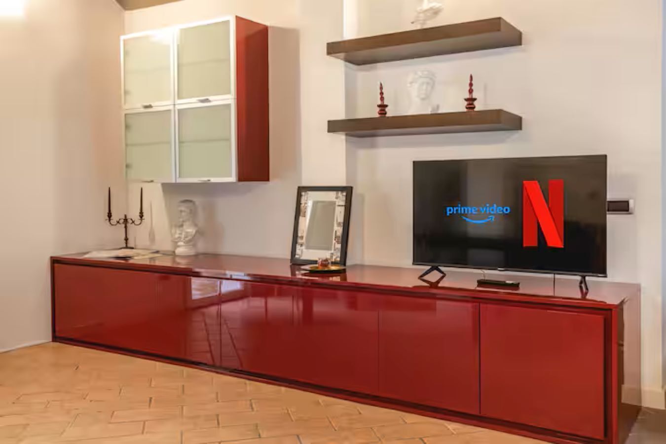 A modern living room with a red entertainment unit, a flat-screen TV displaying the Netflix logo, and a fireplace with decorative items.